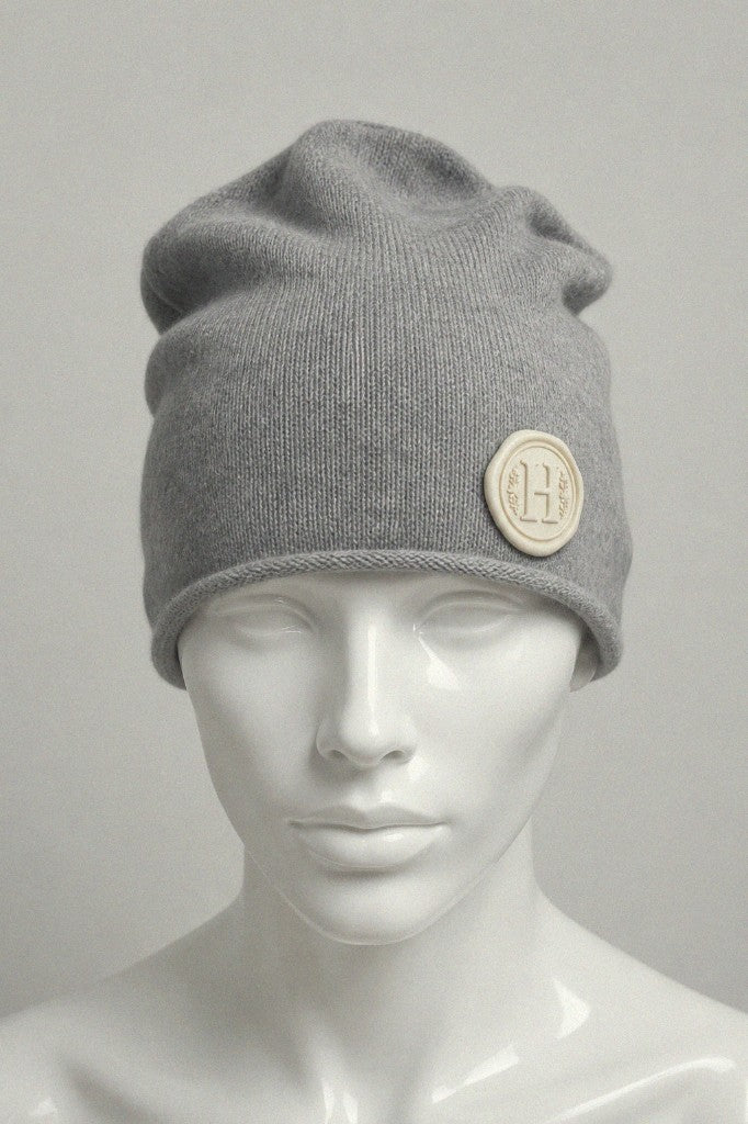 Grey melange Letter Seal Beanie with beige wax-seal letter H badge on cuff — front view on mannequin